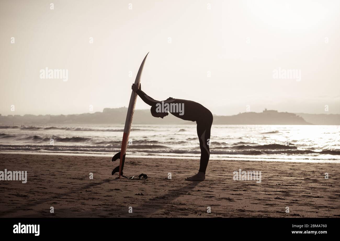 Silhouette des Surfers mit Surfbrett vor oder nach dem Surfen auf den Wellen. Rückansicht des starken Surfmanns am Strand bei Sonnenuntergang oder Sonnenaufgang. Extrem Stockfoto