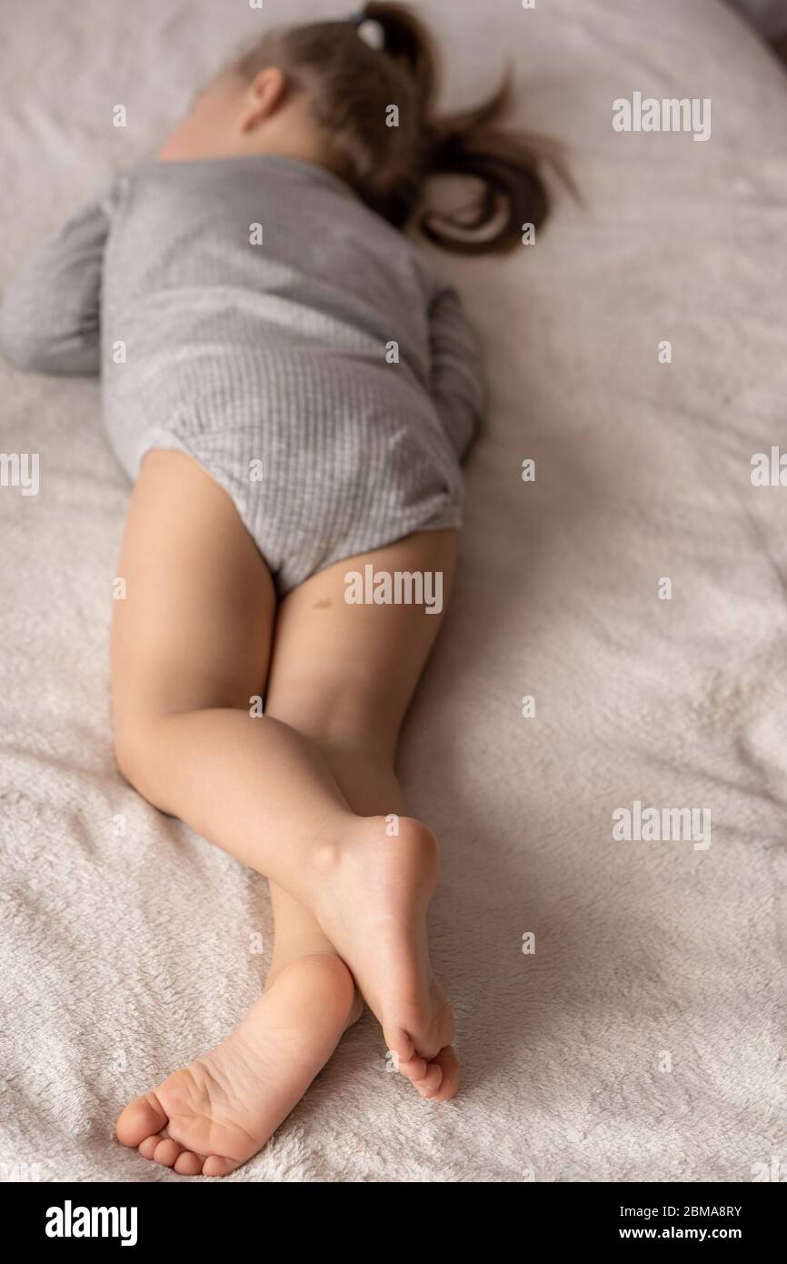Kindheit, Schlaf, Entspannung, Familie, Lifestyle-Konzept - kleines schlafendes Mädchen 3 Jahre alt auf dem Bauch liegend mit gekreuzten Beinen. Stockfoto