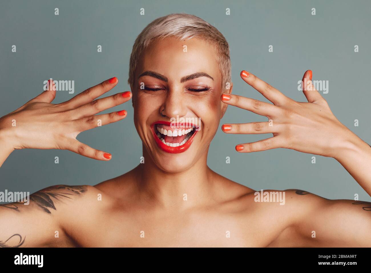 Aufgeregt Frau zeigt ihr Make-up. Weibliches Modell mit Lippenstift und Nagelfarbe lächelnd vor grauem Hintergrund. Stockfoto