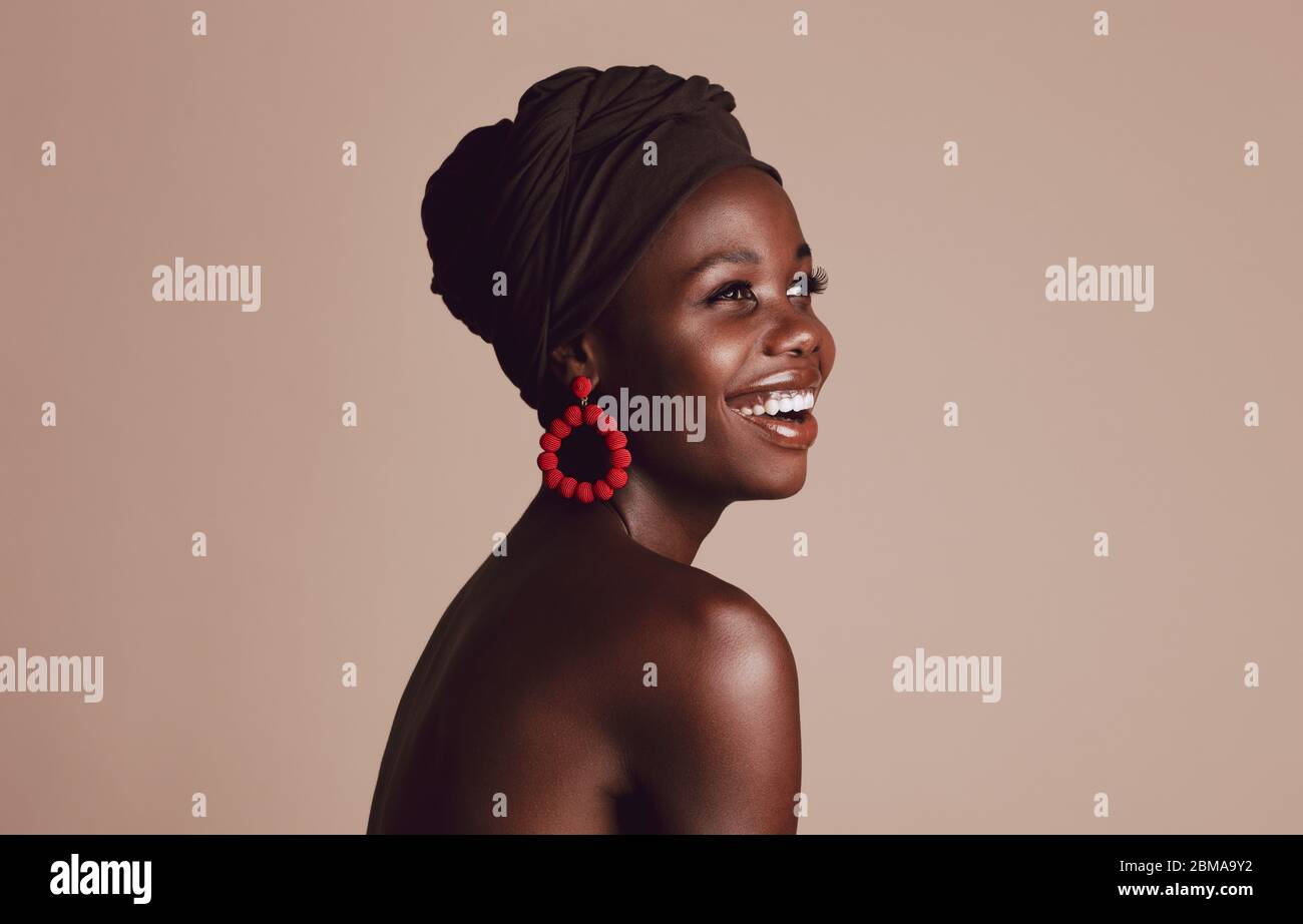 Nahaufnahme von lächelnden afrikanerin auf beigem Hintergrund. Schönes weibliches Modell mit einem Tuch auf dem Kopf gewickelt, wegschauen und lächelnd. Stockfoto