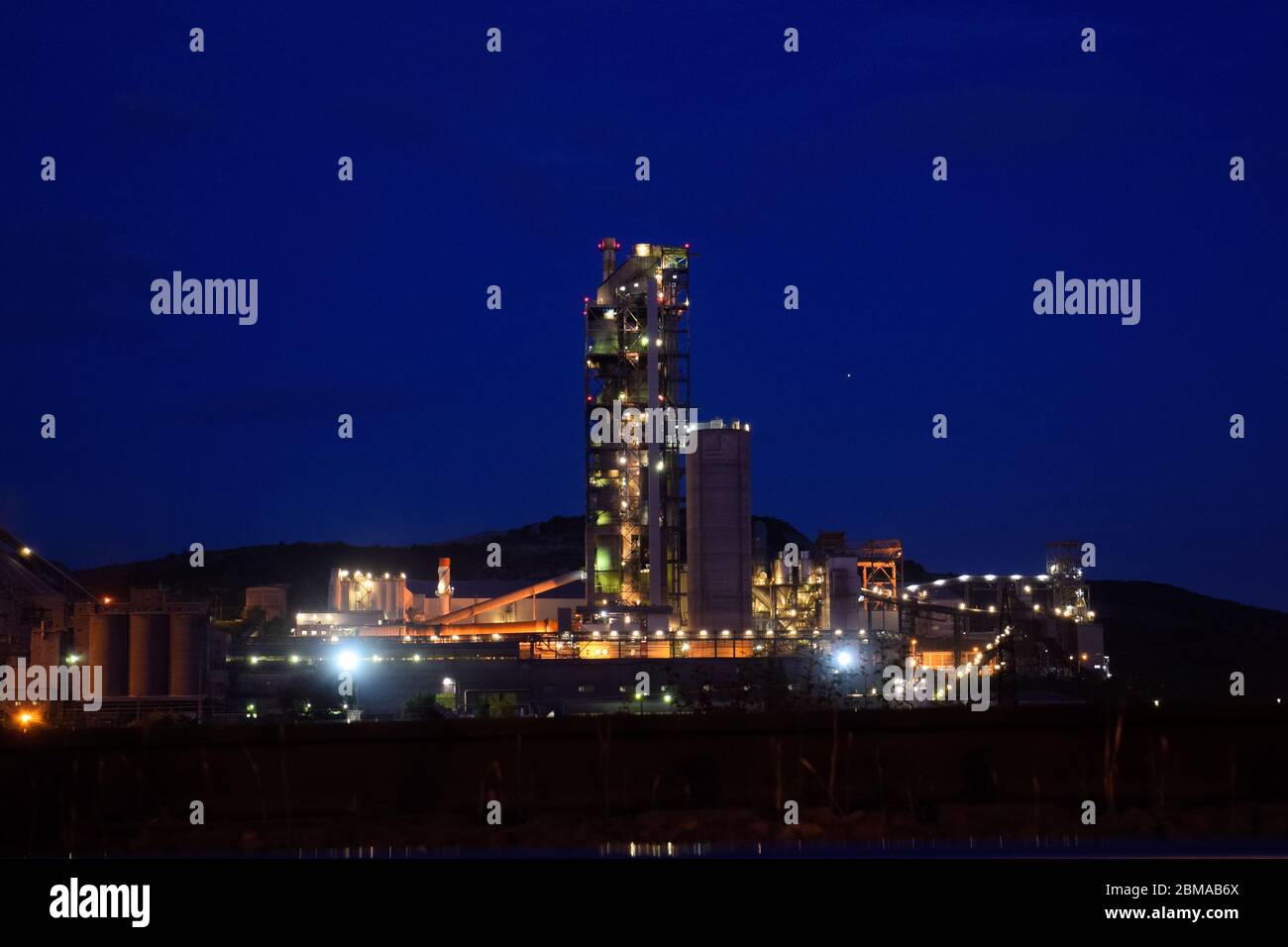 Das Gebäude einer Zementfabrik in der Nacht, die Lichter einer Lampe, die eine Fabrik beleuchtet. Industrieanlage. Stockfoto