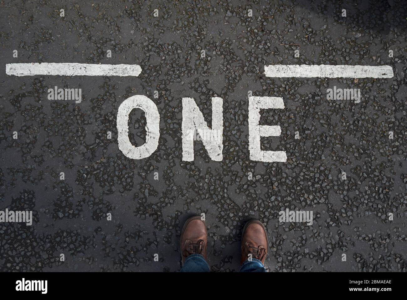Straßenmarkierung mit dem Wort "eins" und den Füßen des männlichen Fotografen. Konzept Einsamkeit, allein. Stockfoto