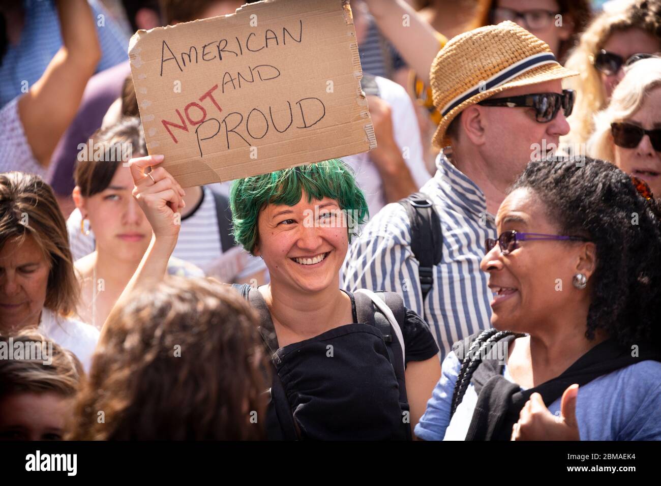 Eine Frau mit gefärbtem grünem Haar, die ein Schild mit der Aufschrift "Amerikaner und nicht stolz" auf dem Protest und der Demonstration gegen Donald Trumps Besuch in London hält Stockfoto
