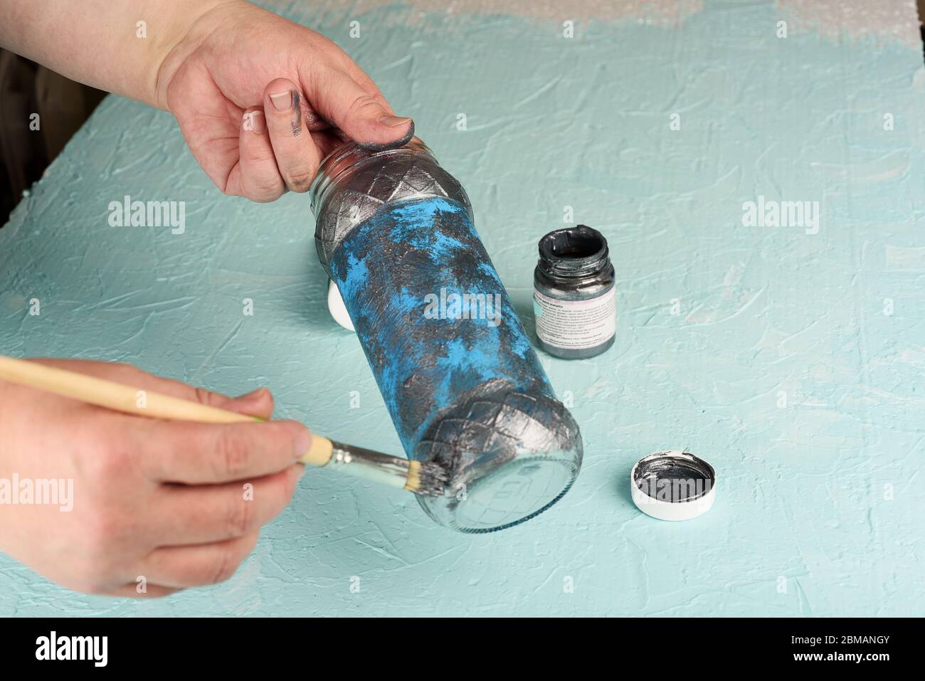 Färbung ein Glas mit grauer Acrylfarbe. Pinsel in die Hand einer Frau malen. Malen Sie auf die Finger. Stockfoto