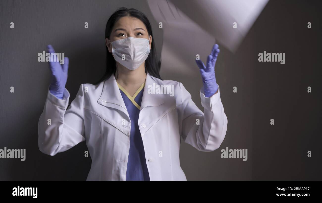 Glücklicher Arzt freut sich über das Ende der Pandemie. Schöne Ärztein lacht, wenn sie auf grauem Hintergrund medizinische Formulare aus Papier wirft Stockfoto