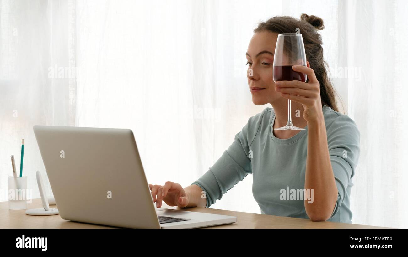 Frau, die mit einem Glas Wein an einem Laptop arbeitet Stockfoto