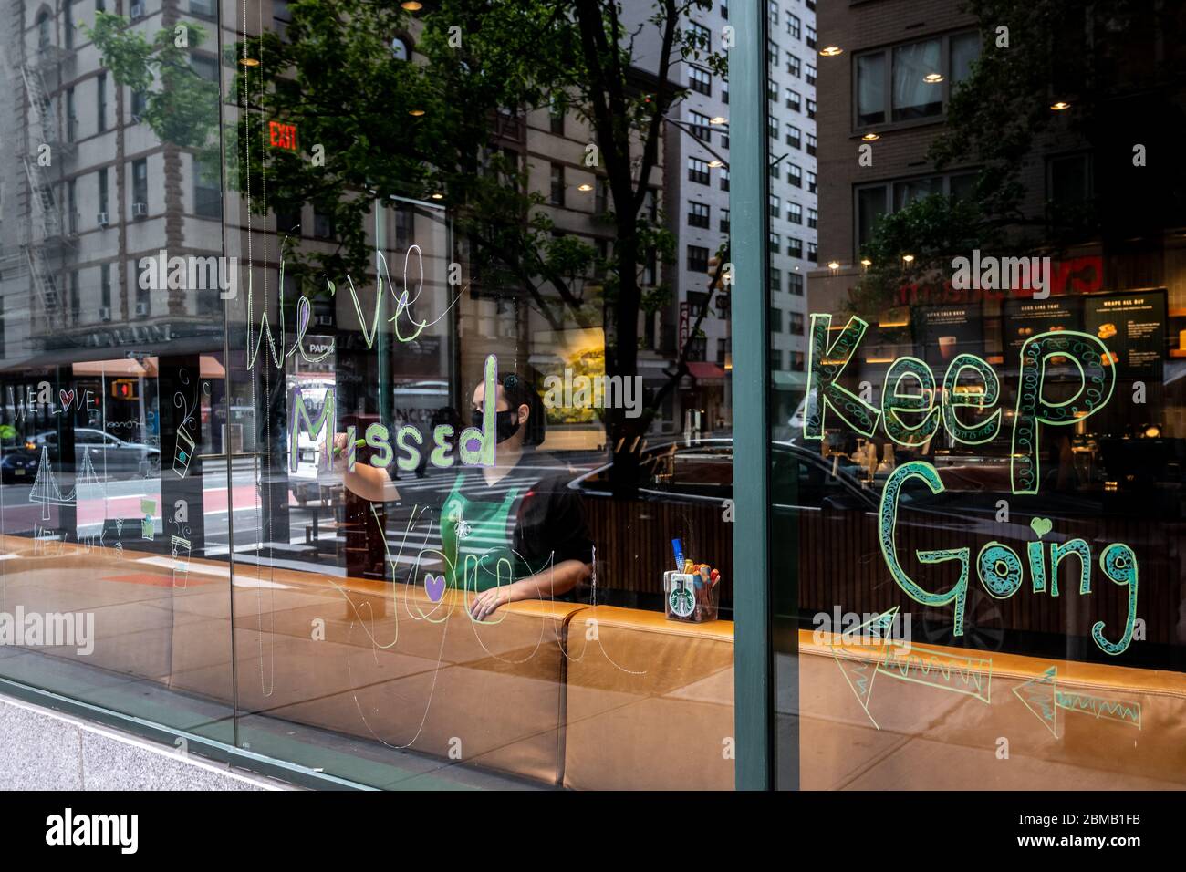 New York, USA. Mai 2020. Ein Starbucks Mitarbeiter trägt eine Gesichtsmaske, wenn sie im Coffee Shop-Fenster der Upper East Side ein Schild mit der Aufschrift „Wir haben dich verpasst“ malt, da sie erst nach über einem Monat, nachdem sie aufgrund der COVID-19-Krise geschlossen wurde, wieder für Take-Outs geöffnet werden. Kredit: Enrique Shore/Alamy Live News Stockfoto