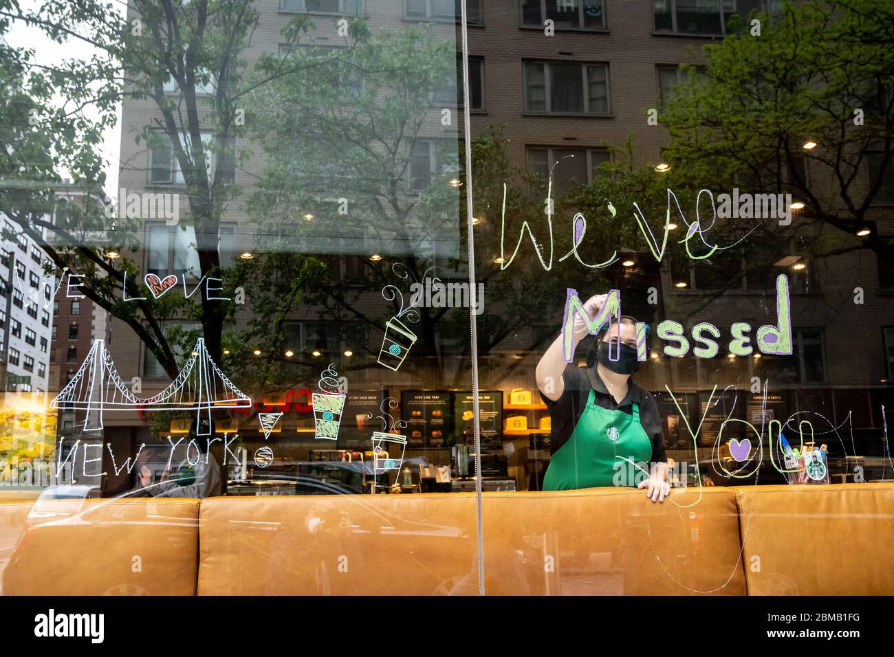 New York, USA. Mai 2020. Ein Starbucks Mitarbeiter trägt eine Gesichtsmaske, wenn sie im Coffee Shop-Fenster der Upper East Side ein Schild mit der Aufschrift „Wir haben dich verpasst“ malt, da sie erst nach über einem Monat, nachdem sie aufgrund der COVID-19-Krise geschlossen wurde, wieder für Take-Outs geöffnet werden. Kredit: Enrique Shore/Alamy Live News Stockfoto