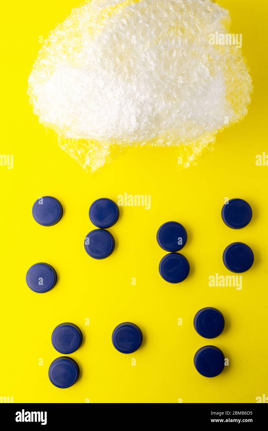Konzeptionelles Foto von Plastikblasen, die eine Wolke darstellen, und blauen Flaschenverschlüssen, die Regenwasser auf gelbem Hintergrund darstellen. Recycling von Kunststoff in den Stockfoto