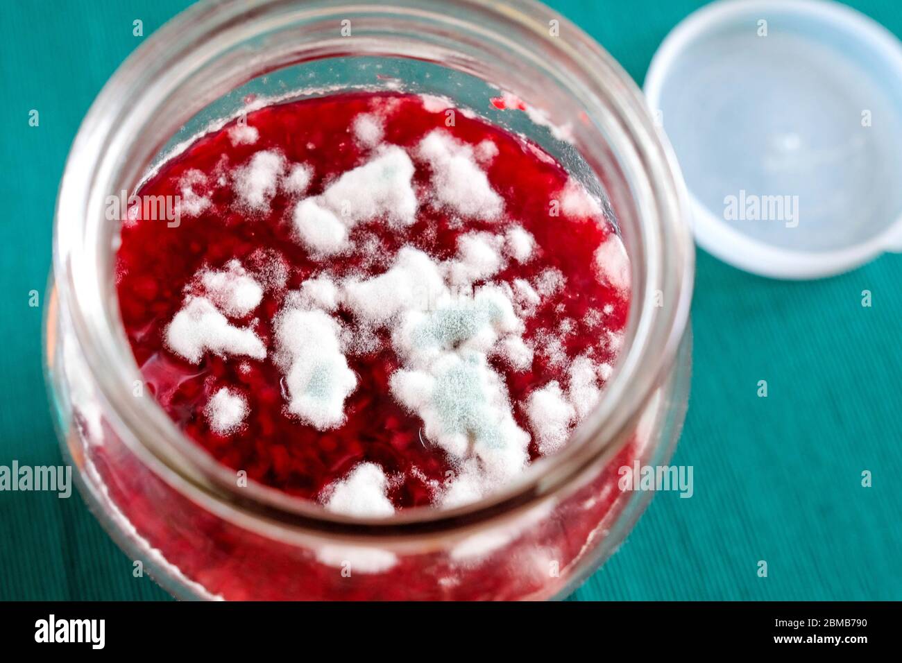 Weiß-grüne Form für Marmelade. Verdorbene Marmelade. Produkt in einem Glas, Nylon-Kappe, verschwommener Hintergrund. Stockfoto