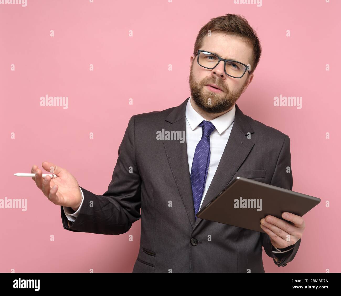 Ein seriöser Geschäftsmann im Anzug arbeitet mit Tablet und Stylus, macht einen Bericht oder eine Präsentation und schaut fragend auf die Kamera. Stockfoto