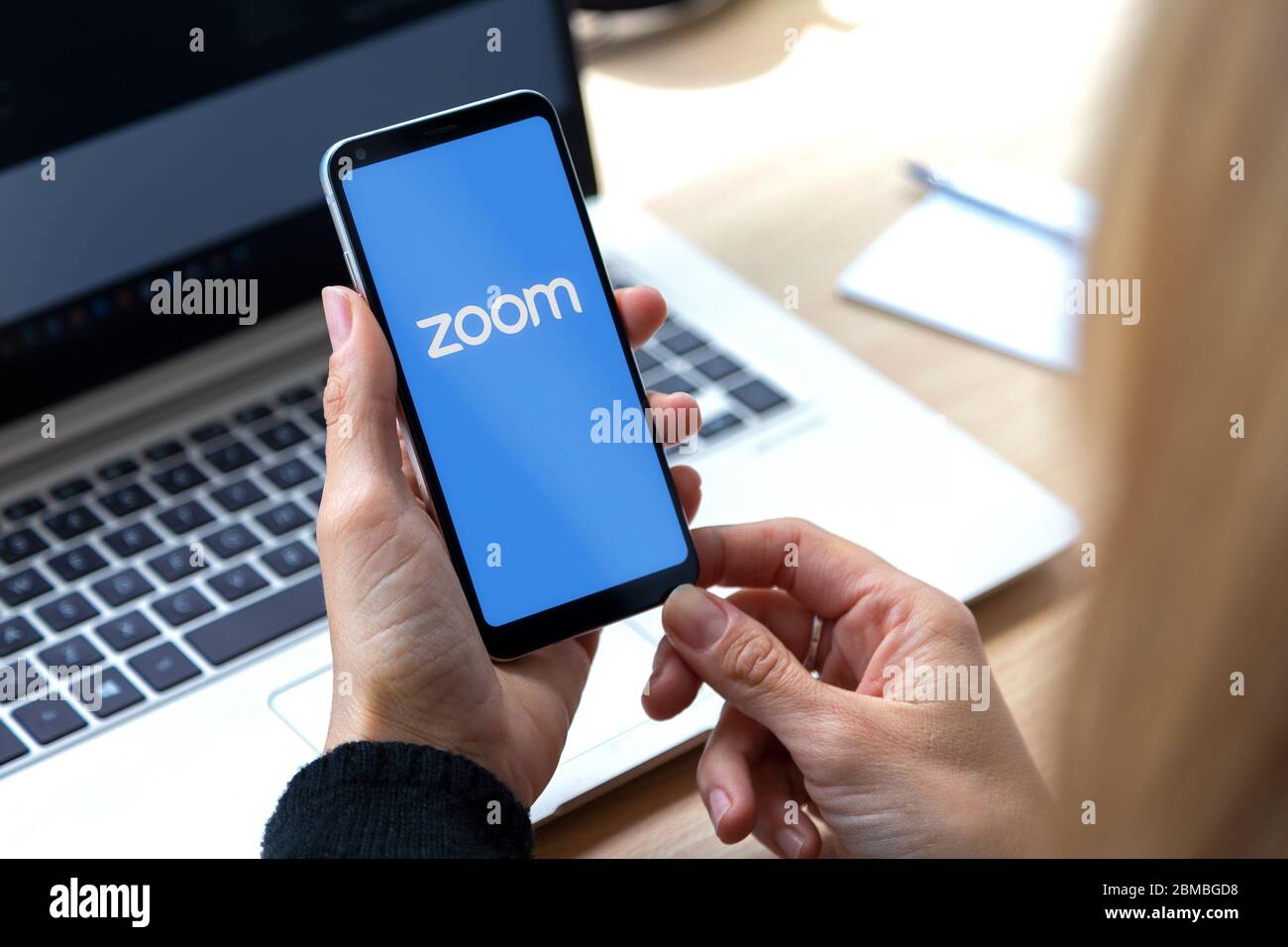 Zoom-App für Smartphone. Frau mit Telefon in den Händen und einem Logo der Videokonferenz-Anwendung auf dem Bildschirm dieser. Stockfoto