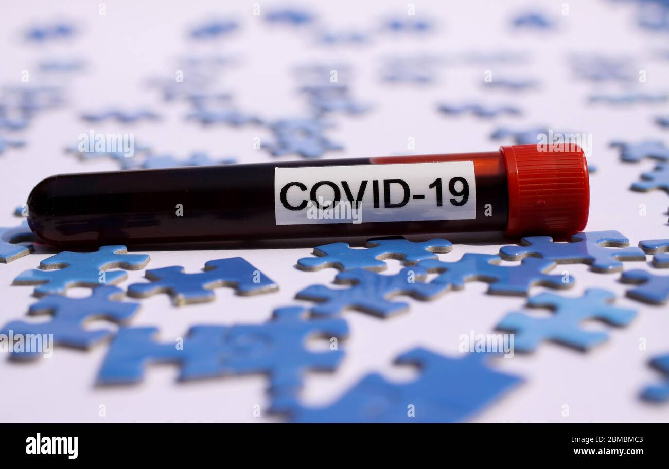 Wirtschaftliche Erholung und Wiederaufbau Konzept: Isolierte Covid-19 Blutprobe Fläschchen auf verstreuten blauen Puzzleteile Stockfoto