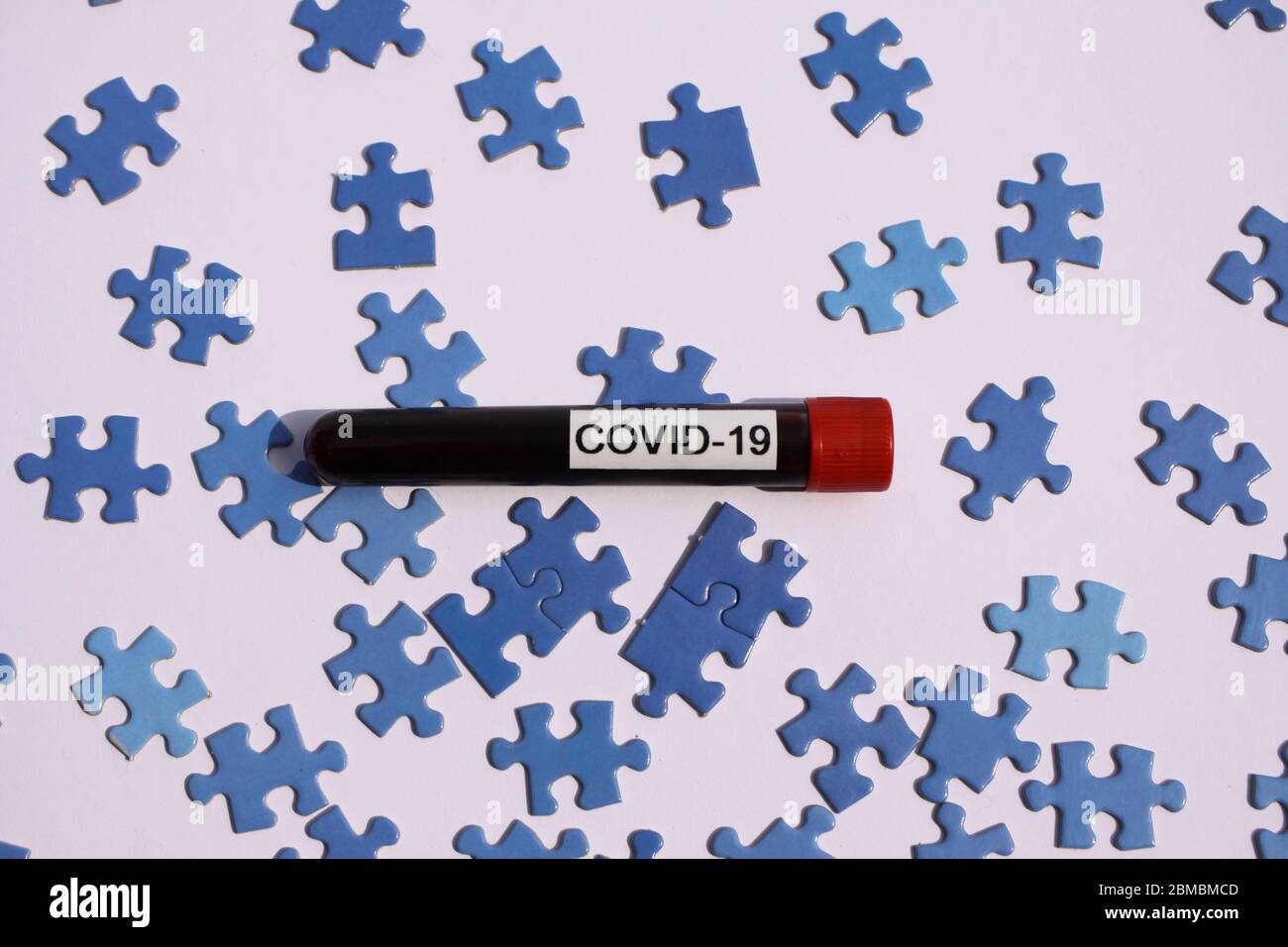 Wirtschaftliche Erholung und Wiederaufbau Konzept: Isolierte Covid-19 Blutprobe Fläschchen auf verstreuten blauen Puzzleteile Stockfoto