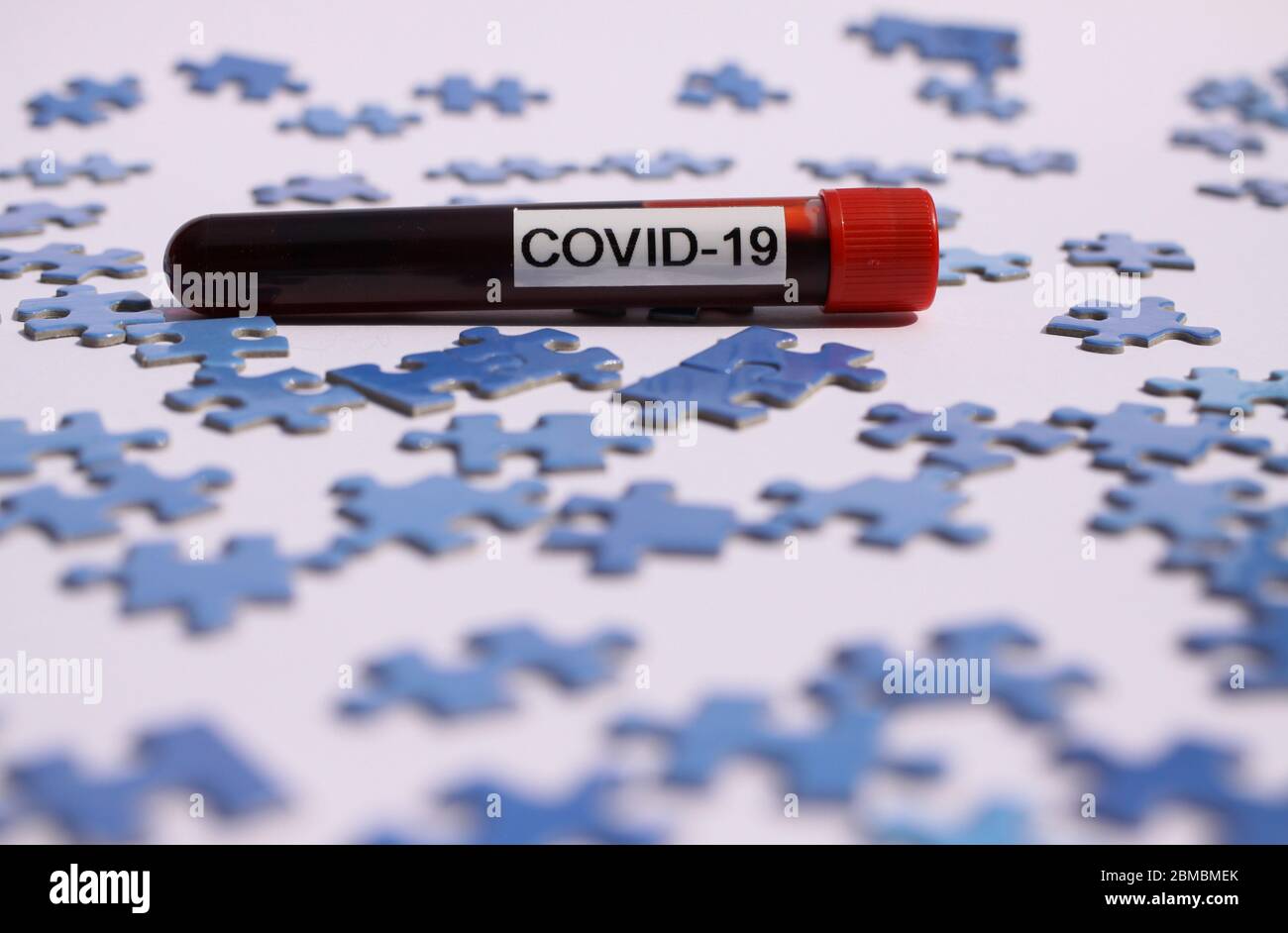Wirtschaftliche Erholung und Wiederaufbau Konzept: Isolierte Covid-19 Blutprobe Fläschchen auf verstreuten blauen Puzzleteile Stockfoto