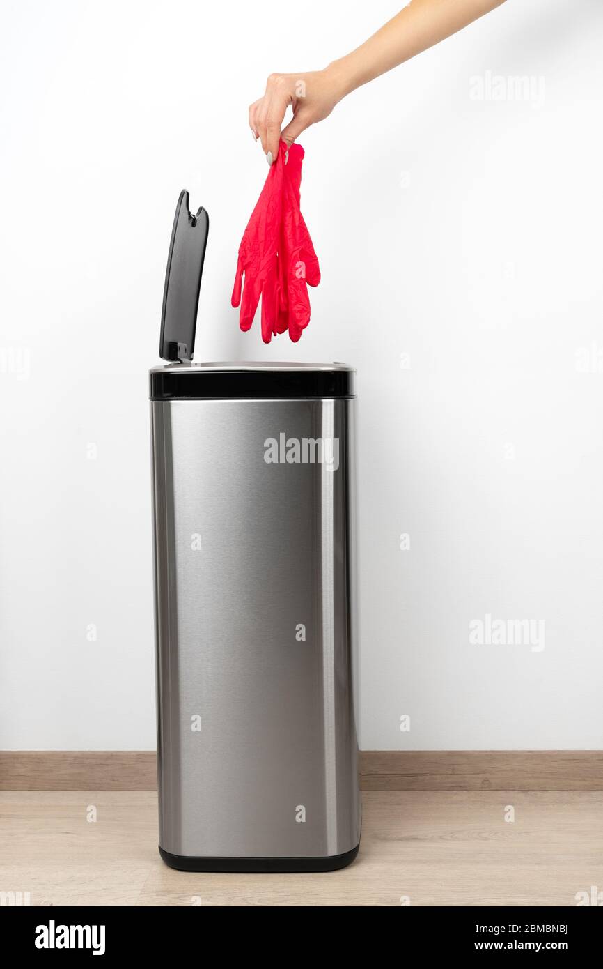Weibliche Hand wirft auf grauem Hintergrund einen pinken Schutzhandschuh in den Mülleimer. Stockfoto
