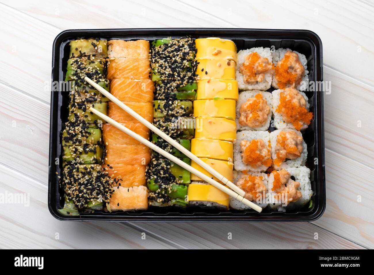 Set von Sushi-Brötchen mit Lachs und Gemüse in schwarzem Tablett und Holzstäbchen auf Bretter. Asiatische Gerichte mit Meeresfrüchten. Eine traditionelle japanische Küche, Cu Stockfoto