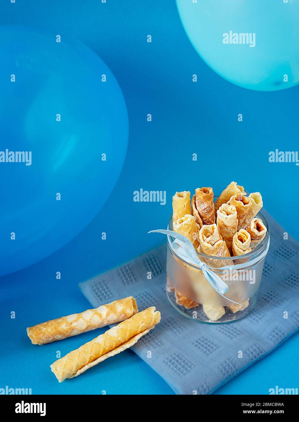 Leckere Waffelbrötchen mit Puderzucker in einer Glasschüssel Mit Luftballons auf blauem Hintergrund Stockfoto