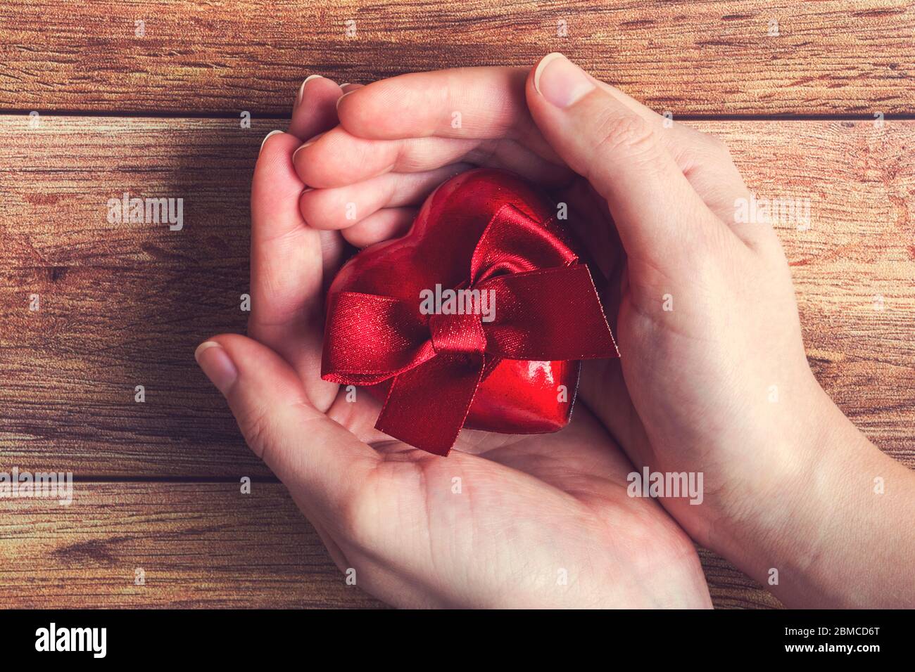 Frau Hände mit einem roten Geschenk Herz mit Schleife auf Holzhintergrund. Valentinstag, Muttertag, Geburtstag, Feier, Geben Stockfoto