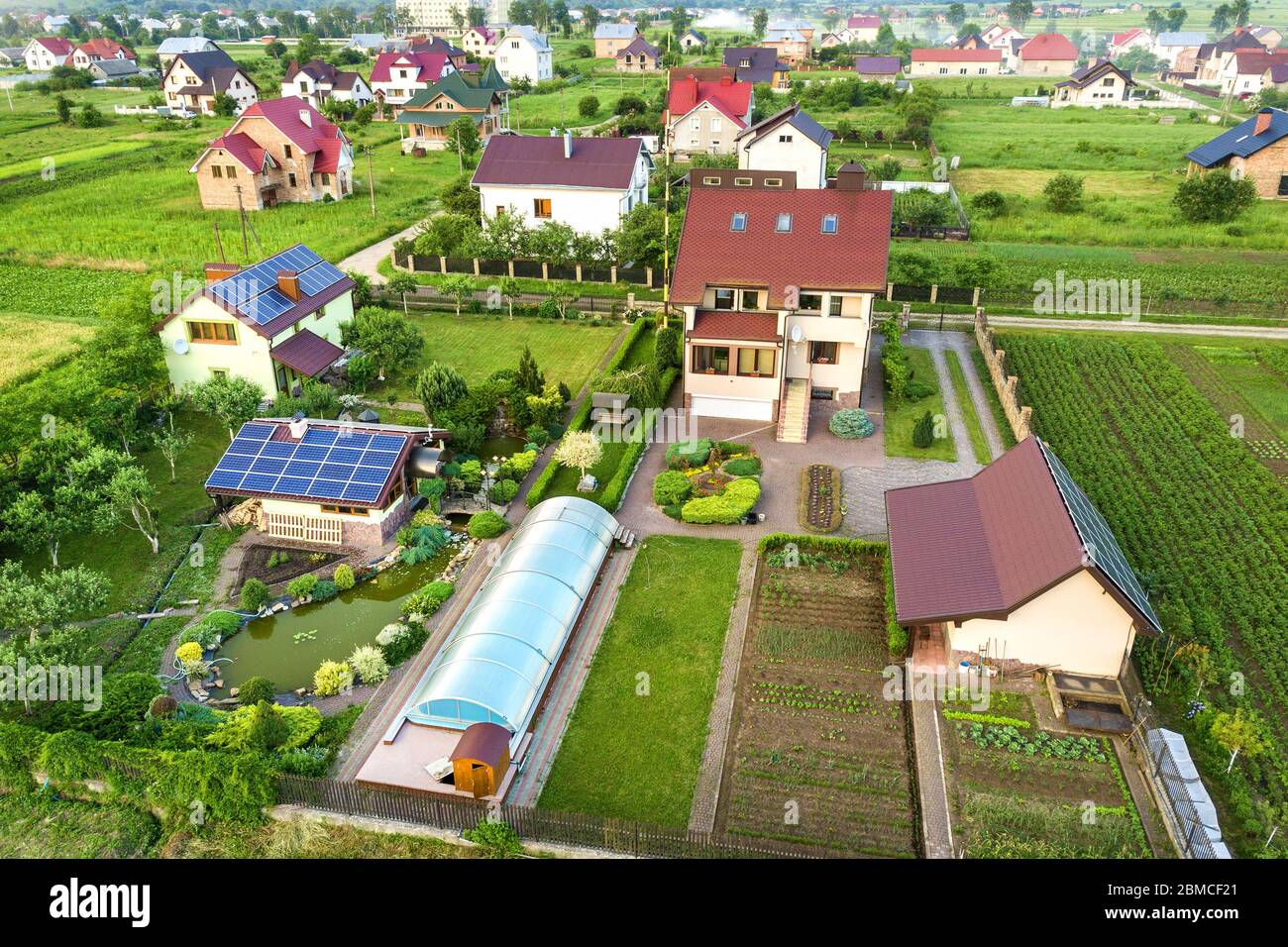 Luftbild eines Privathauses im Sommer mit blauen Sonnenfoto-Voltaikfeldern auf Dach und Grünhof. Stockfoto