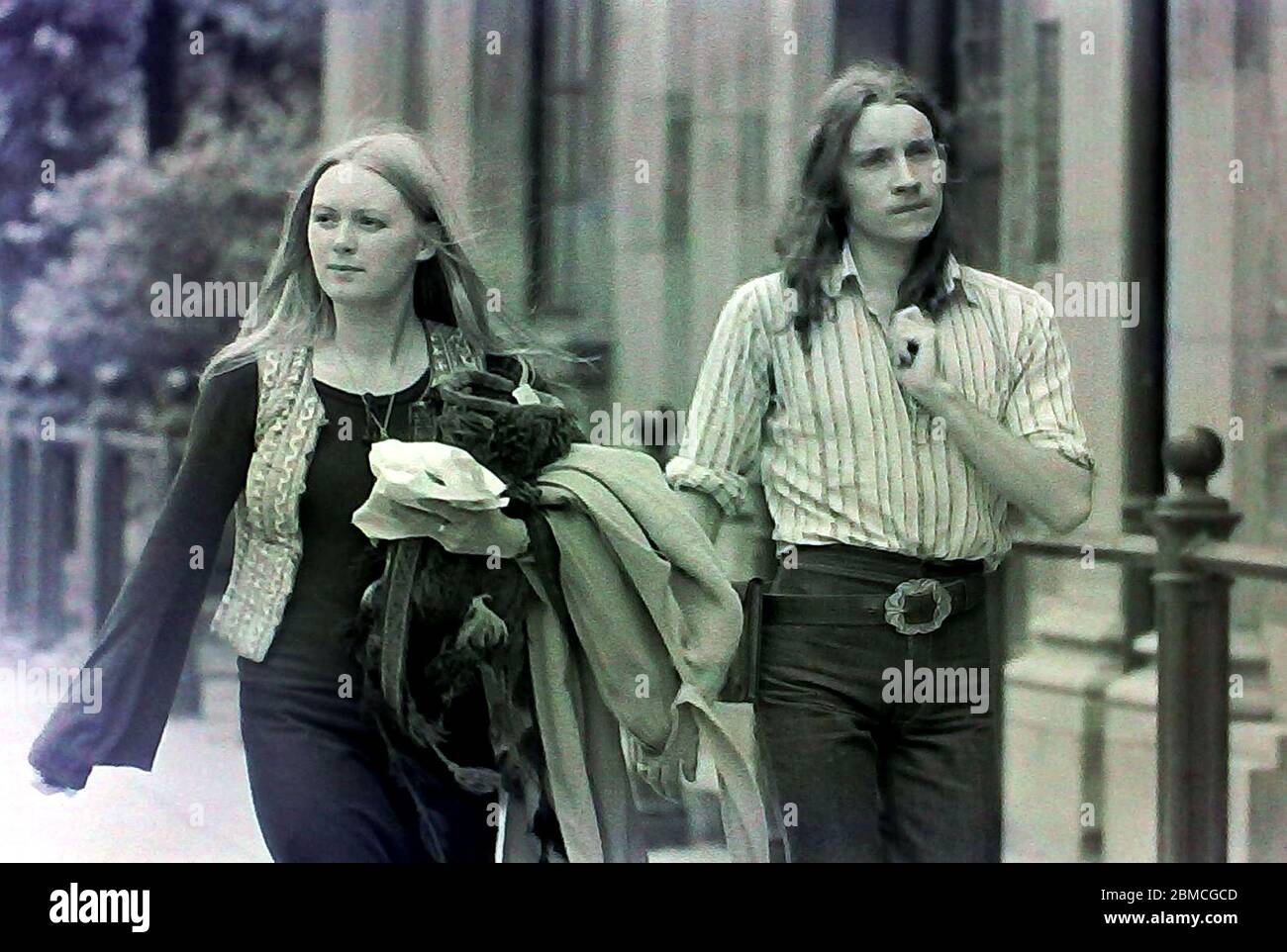 Ein junger Mann und eine junge Frau, die beide lange Haare haben, gehen 1974 in Manchester, England, Großbritannien, entlang einer Straße. Stockfoto