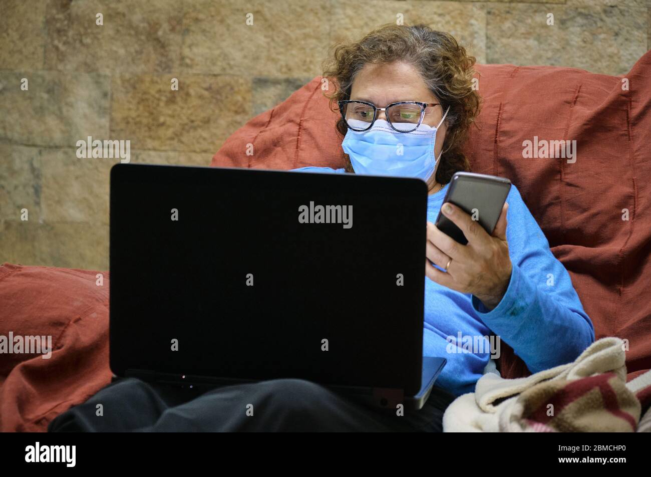 Eine Ärztin Heimarbeit mit einem Notebook und Handy mit einer Gesichtsmaske auf der Couch Stockfoto