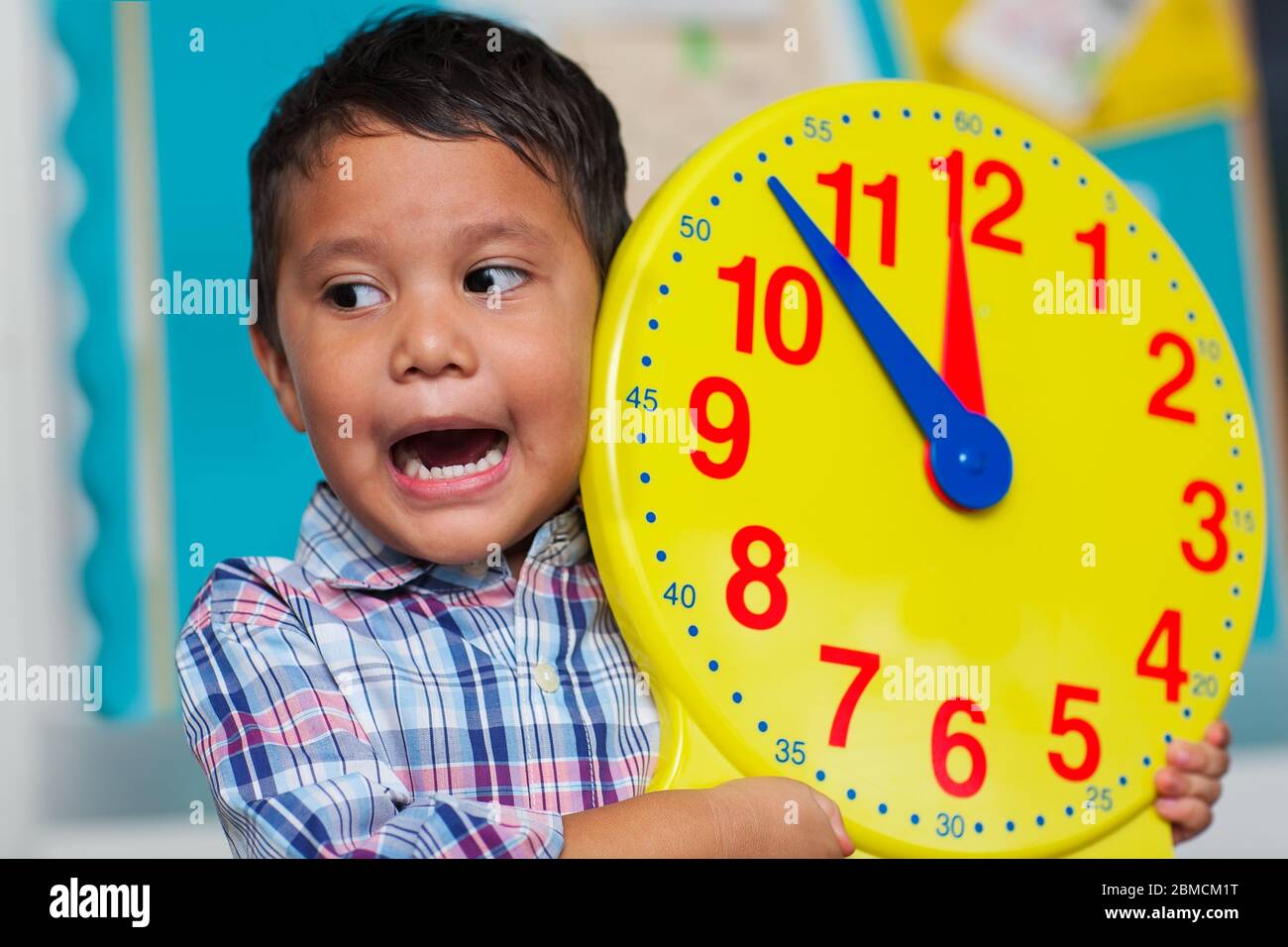 Vorschulalter Junge schreien, was Zeit es ist, während eine große pädagogische analoge Uhr für Kinder halten. Stockfoto