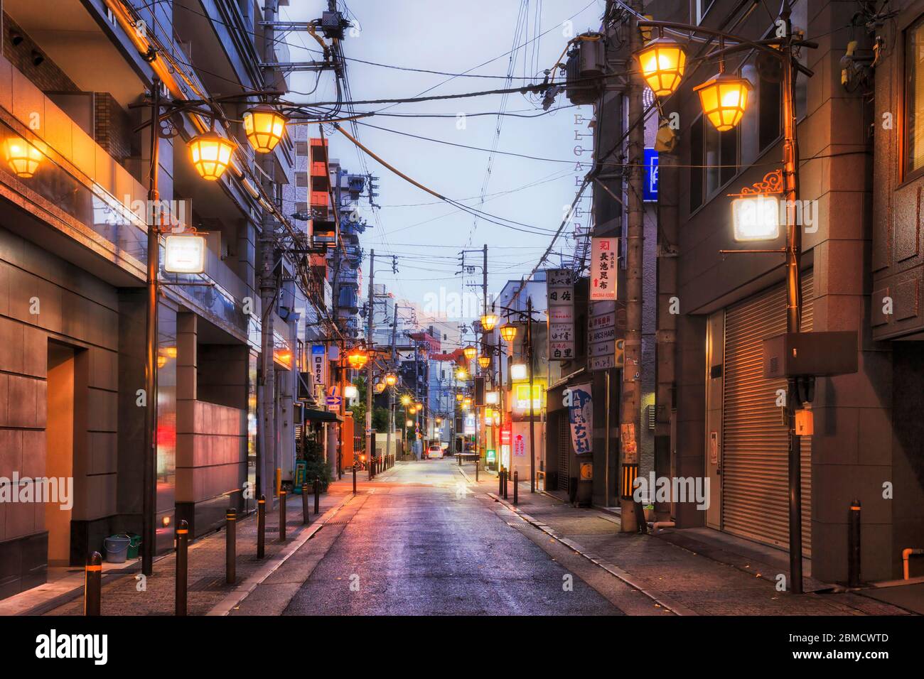 Osaka, Japan - 26 Dez 2019: Ruhige Hintergasse in der Innenstadt von Osaka bei Sonnenaufgang mit Straßenlaternen und verschlossenen Türen lokaler Unternehmen. Stockfoto