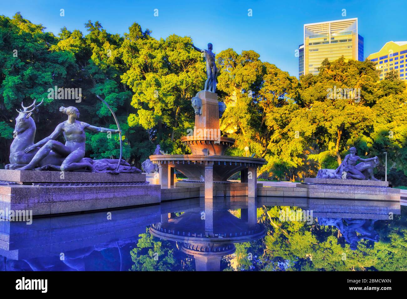Innenstadt von Sydney im Hyde Park um stilles Wasser von Brunnen gegen blauen Himmel von Bäumen umgeben. Stockfoto