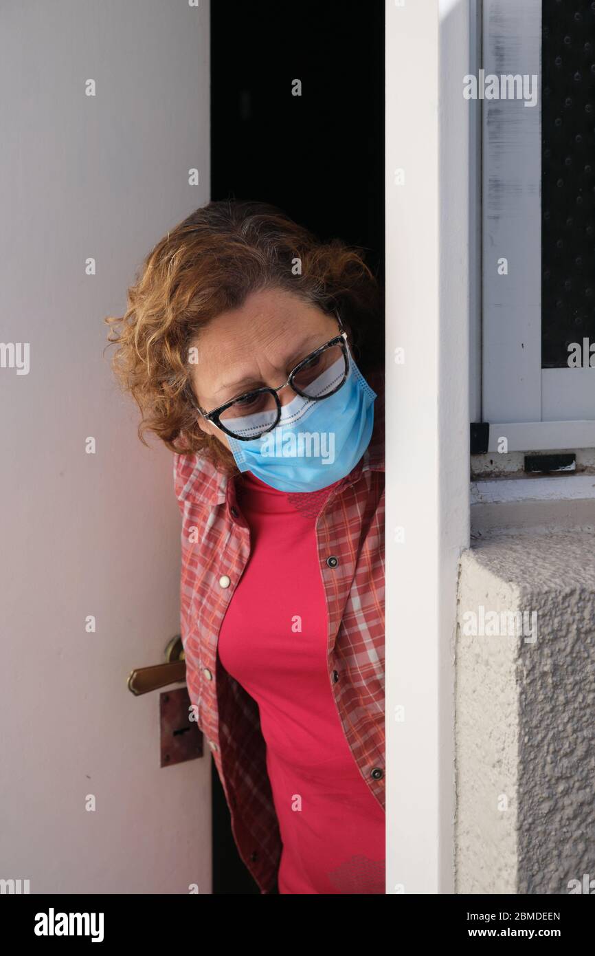 Eine alte Frau, die während der Coronavirus-Pandemie mit einer Gesichtsmaske aus der Tür schaut Stockfoto
