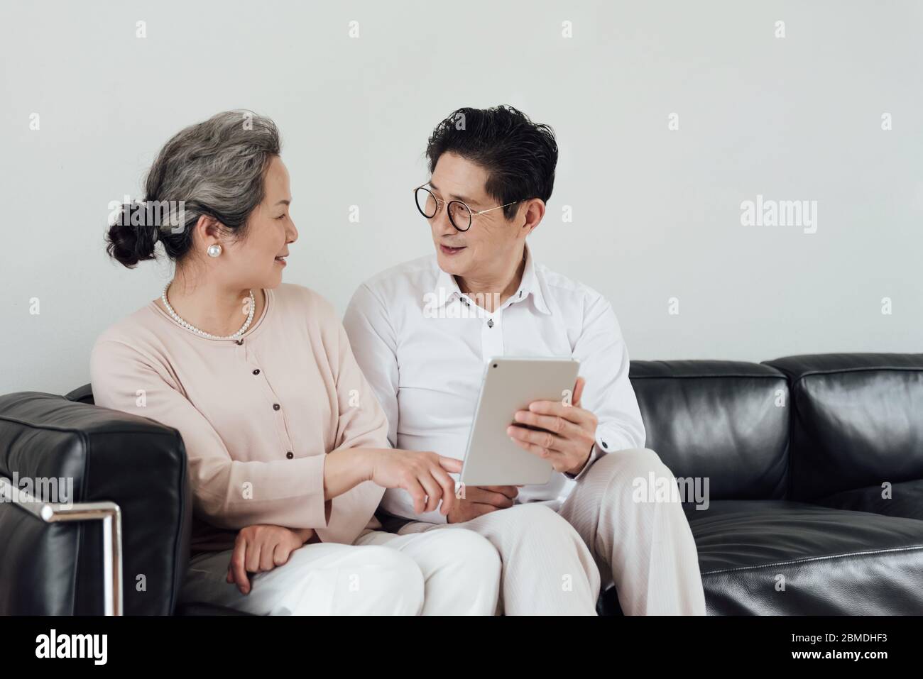 Ein älteres asiatisches Paar, das elektronische Geräte auf dem Sofa benutzt Stockfoto