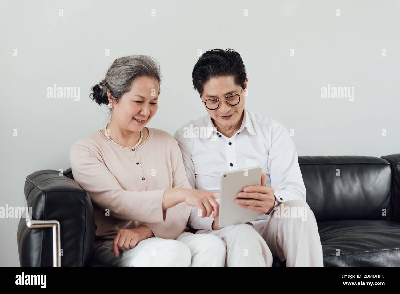 Ein älteres asiatisches Paar, das elektronische Geräte auf dem Sofa benutzt Stockfoto