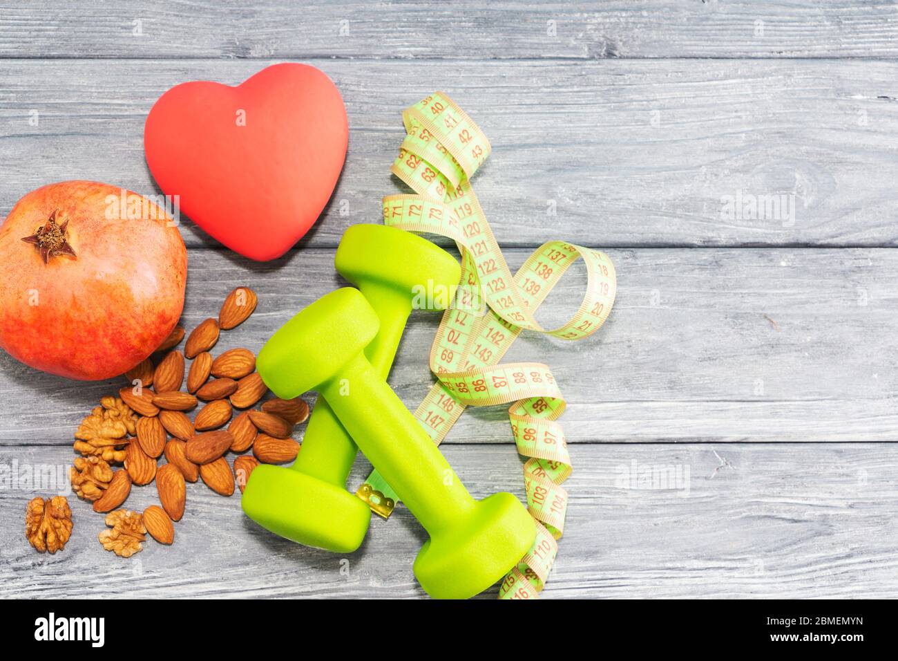 Granatapfel, Hanteln, Maßband auf dem Hintergrund einer Holzstruktur. Fitness, Sporternährung. Stockfoto