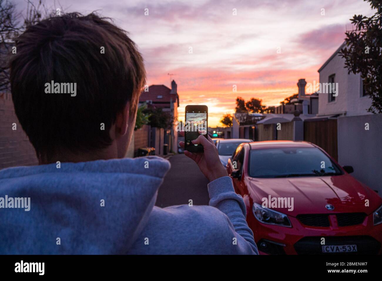 Ein Teenager, der mit seinem Smartphone den Sonnenuntergang fotografiert Stockfoto