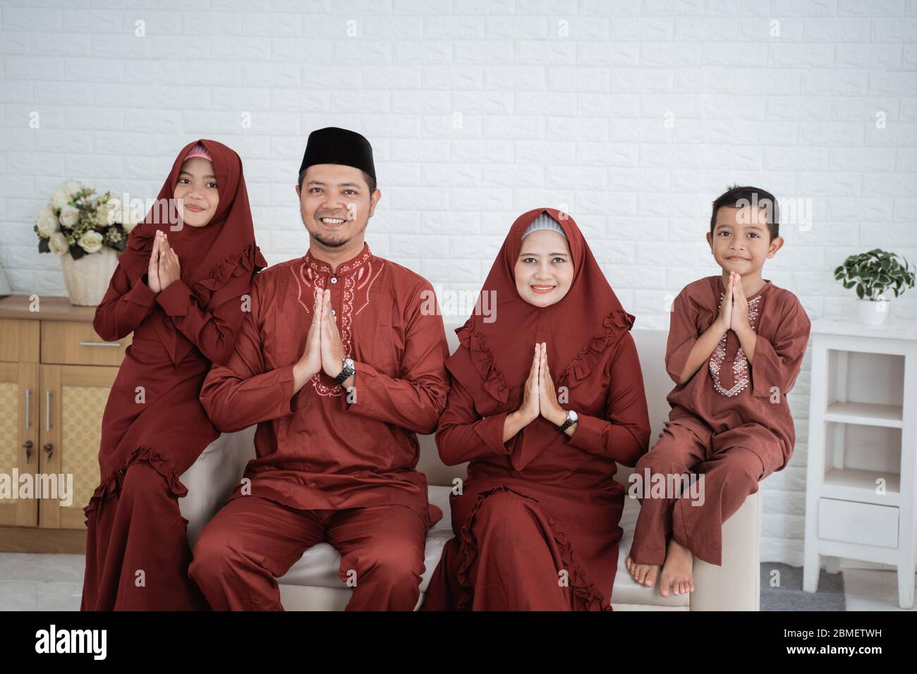 Asiatische muslimische Familie in traditioneller malaiischer Kleidung wünscht Eid Mubarak alles gute, wenn sie zusammen auf dem Sofa sitzt Stockfoto