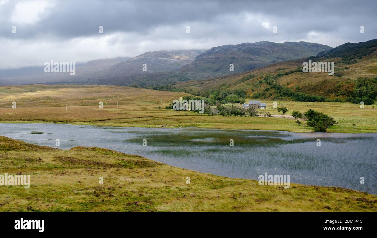 Ein eineineinbands Haus steht neben einem kleinen loch und Fluss unter den Bergen der Northwest Highlands von Schottland. Stockfoto
