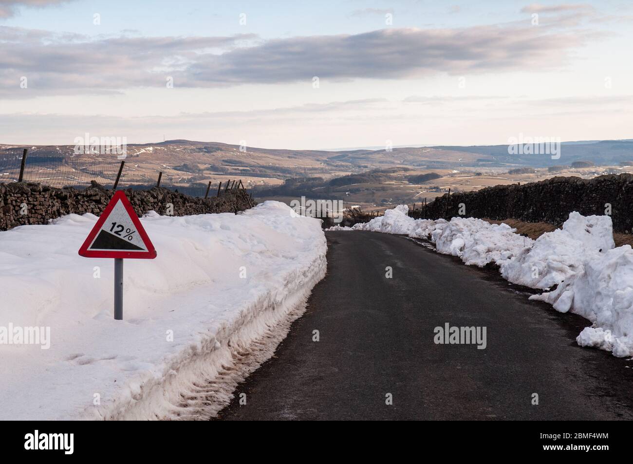 Winterschnee ist auf den Seitenrändern einer steilen Landstraße über den Wald der Bowland Hügel, über dem Hodder Valley bei Slaidburn in Lancashire angehäuft. Stockfoto