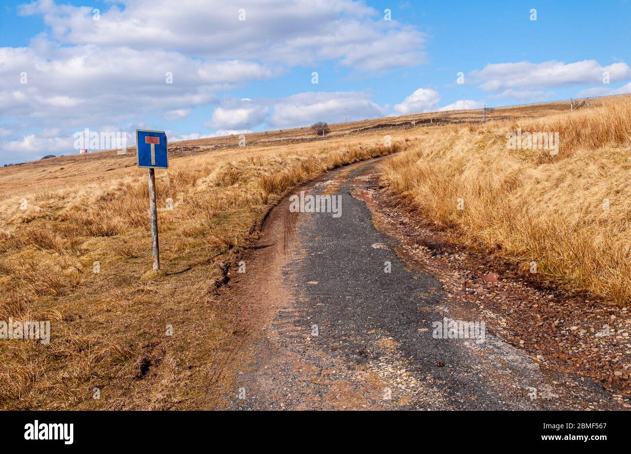 Eine verlassene Straße, die von der Autobahn M6 durchtrennt wird, verläuft durch raues Grasland in Cumbria im Norden Englands. Stockfoto