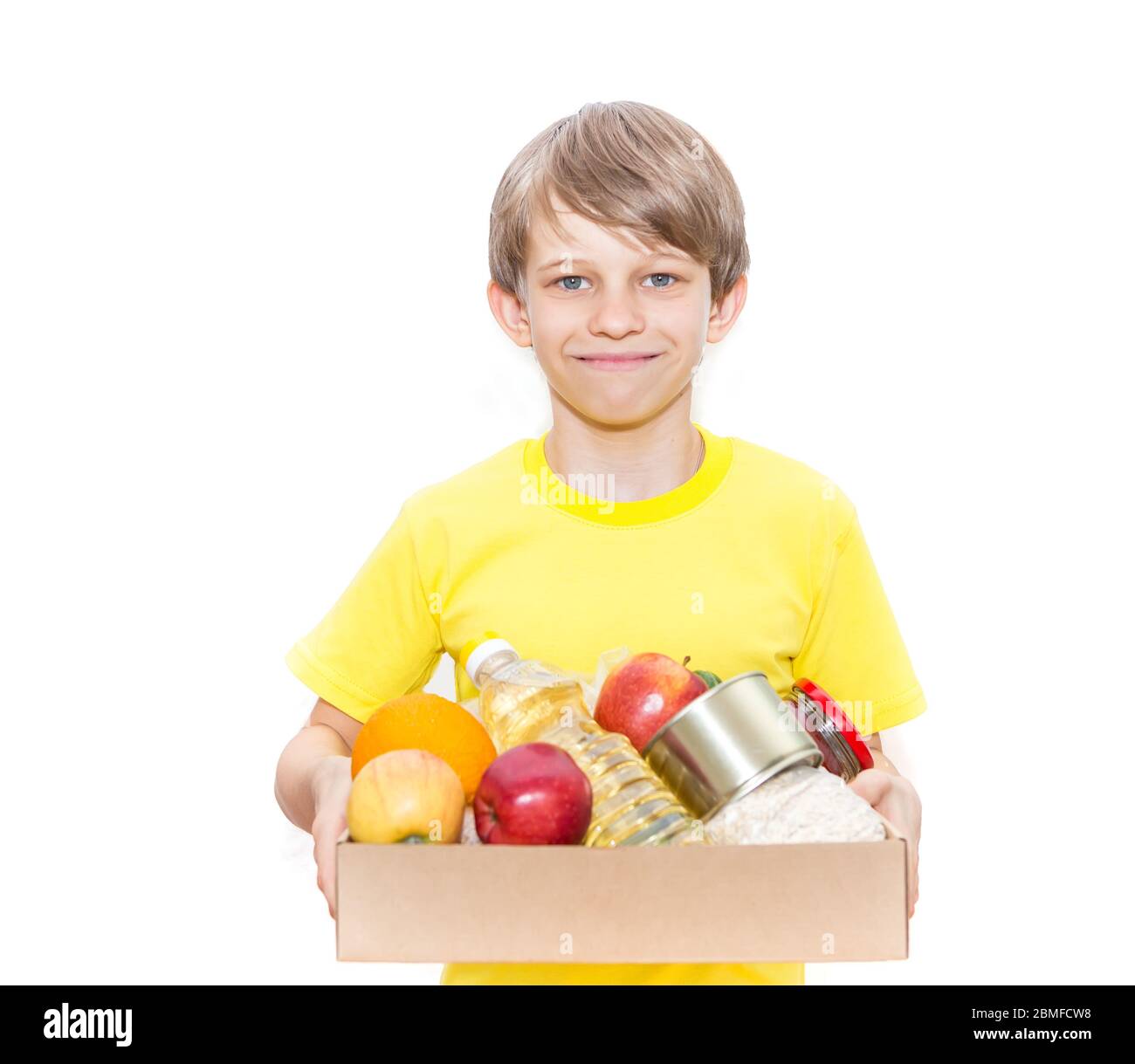 Glücklicher Junge hält eine Kiste mit Nahrung, isoliert auf weißem Hintergrund. Lieferung von Lebensmitteln. Freiwilliger bringt einen Lebensmittelkasten. Stockfoto