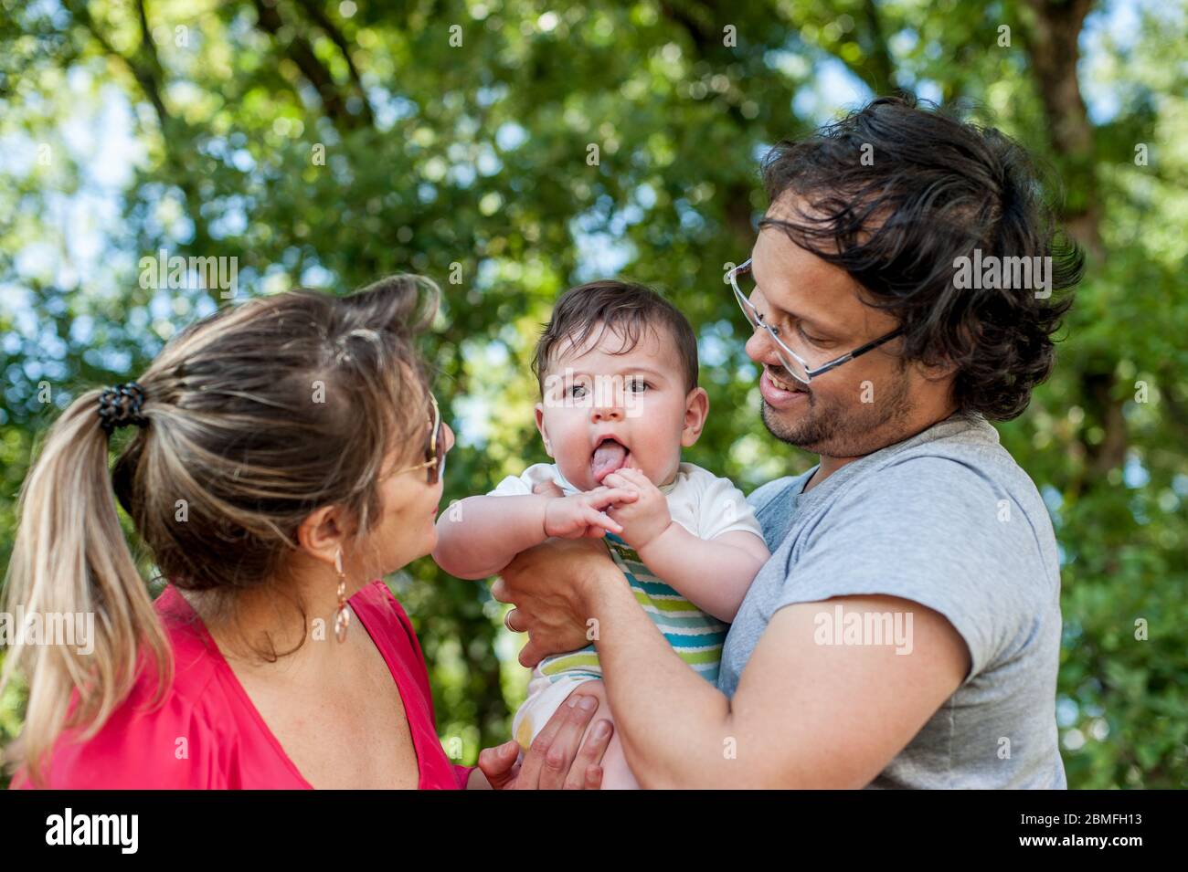 Vorderansicht der glücklichen Eltern, die mit ihrem Baby im Park spielen. Stockfoto