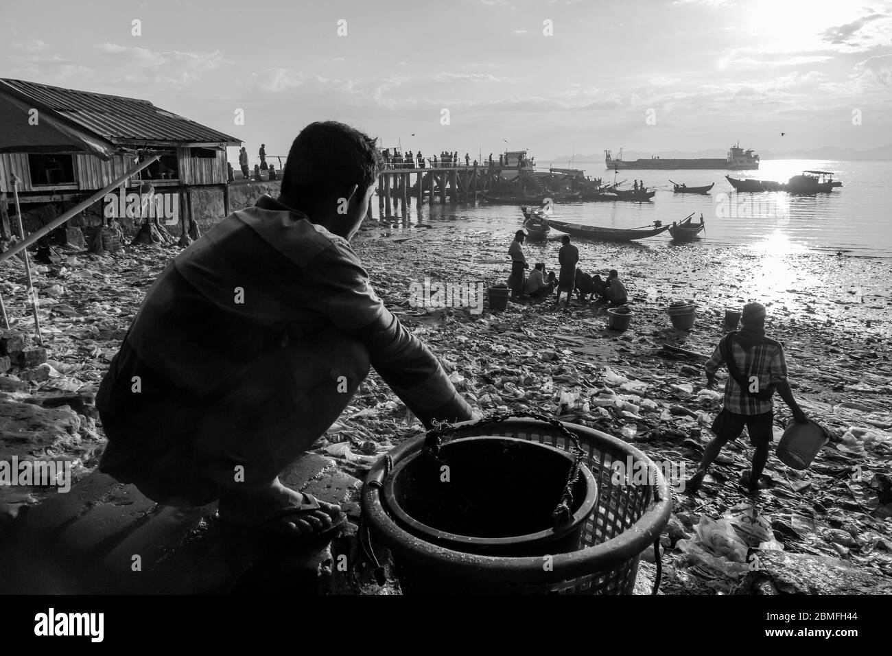 Ebbe und Menschen suchen nach Essbarem oder wiederverwendbarem Material, unter dem Müll, der am Strand gelandet ist. Sittwe, Myanmar Stockfoto