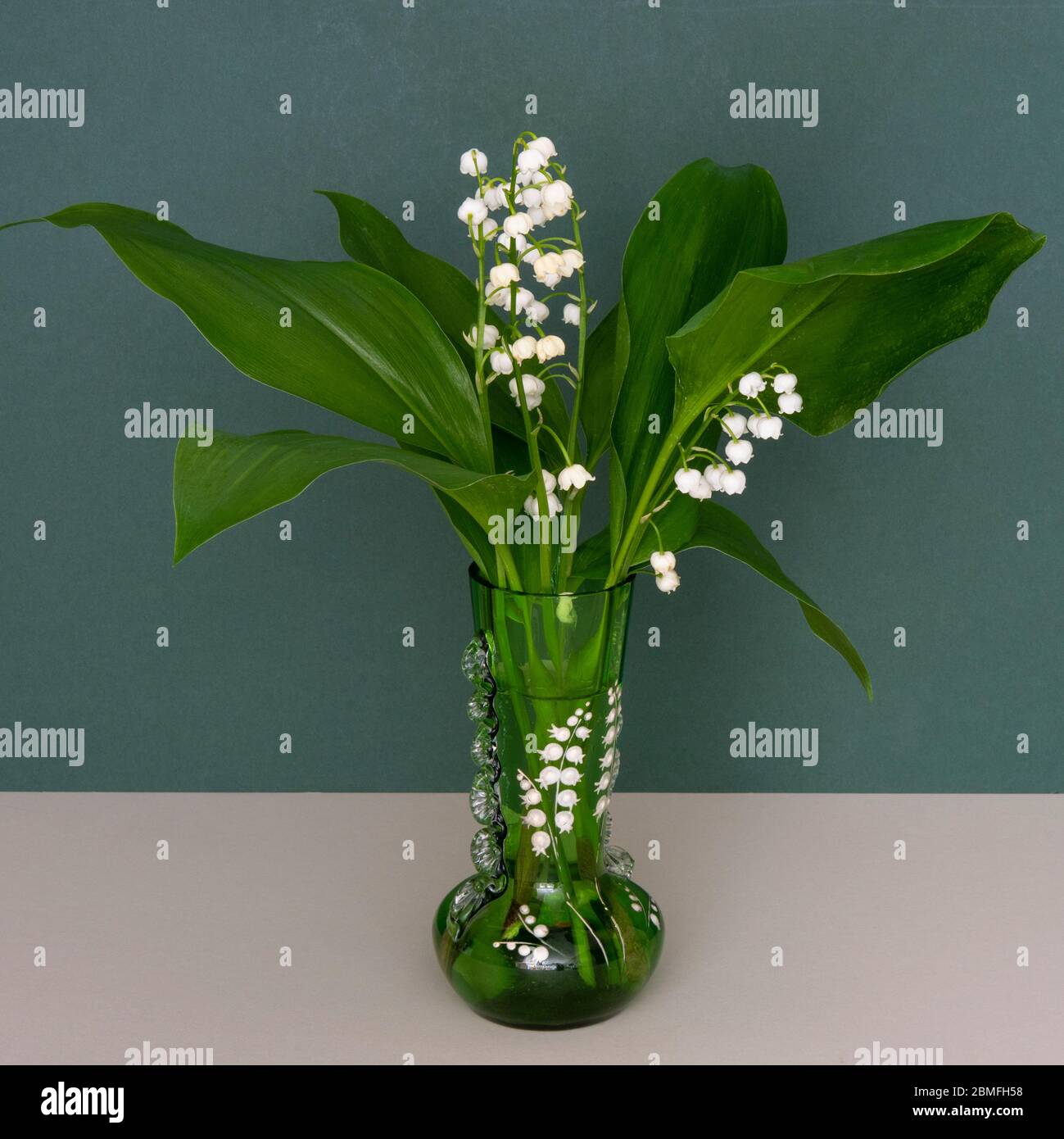 Eine Frühlingsansicht der Maiglöckchen blüht in einer grünen viktorianischen Vase Stockfoto