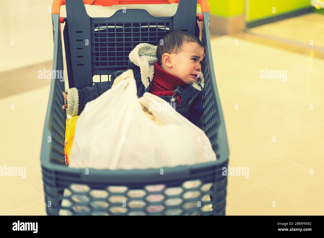 Baby Junge weint in einem Supermarkt in einem Wagen. Das vergessene Kind. Getönte Stockfoto