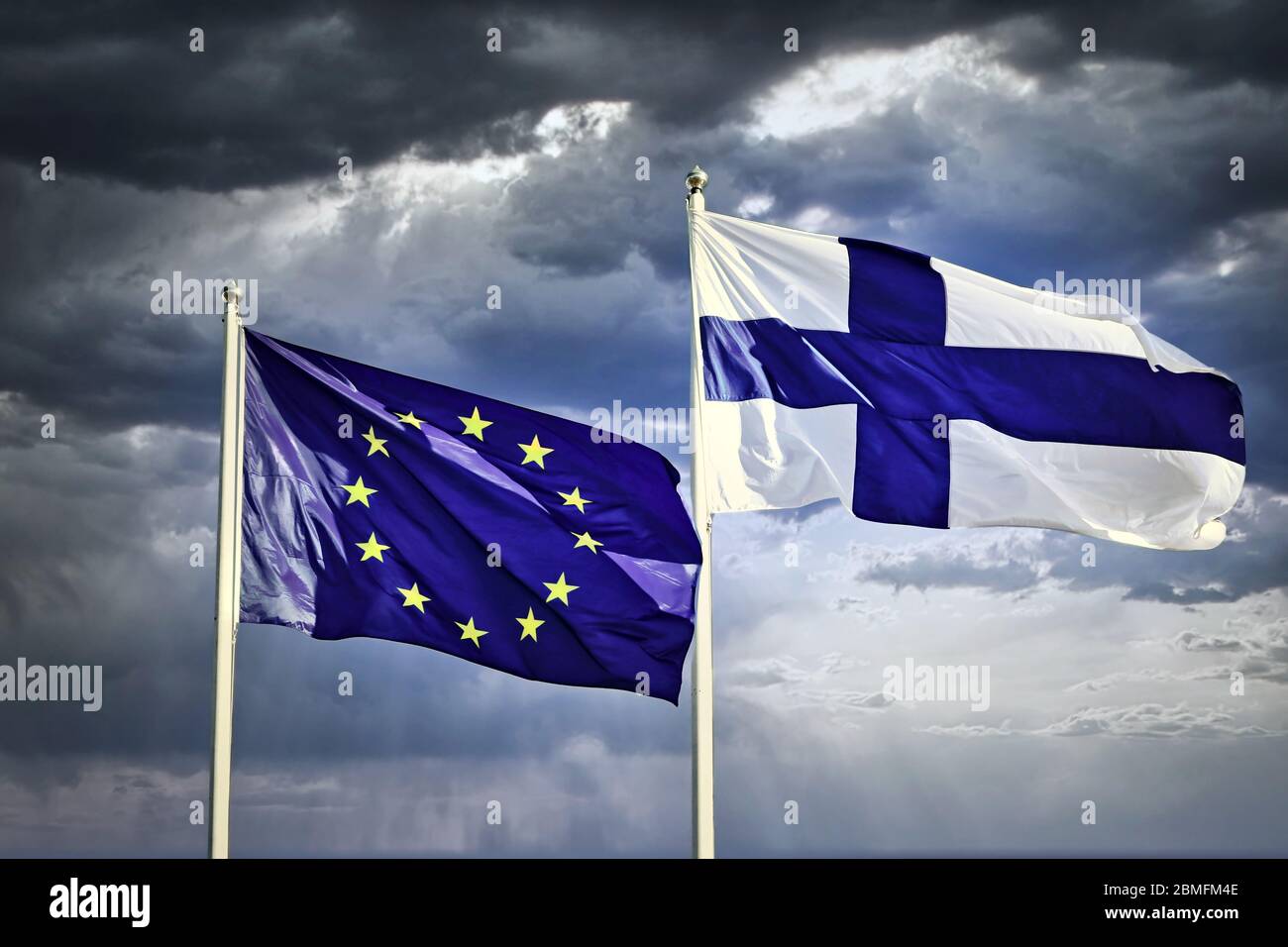 Flaggen der EU und Finnlands vor dramatischem, dunklem und bewölktem Himmel. Stockfoto
