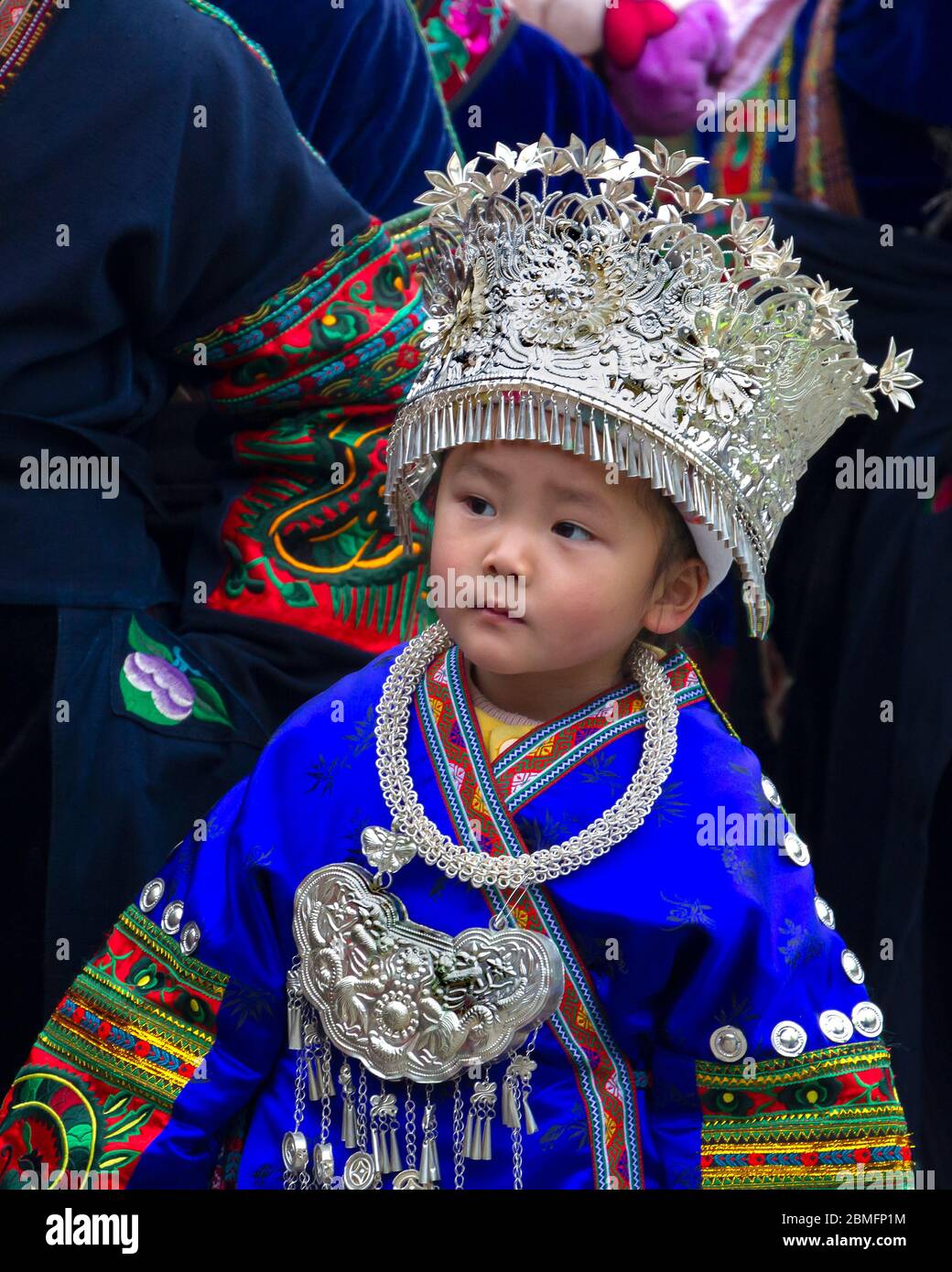 Ein kleiner Junge für einen Moment in der traditionellen ethnischen Tracht einer Frau. Er gehört zu den Longde-Langarmmiao-Minderheitsmenschen. Kaili, Guizhou Provi Stockfoto