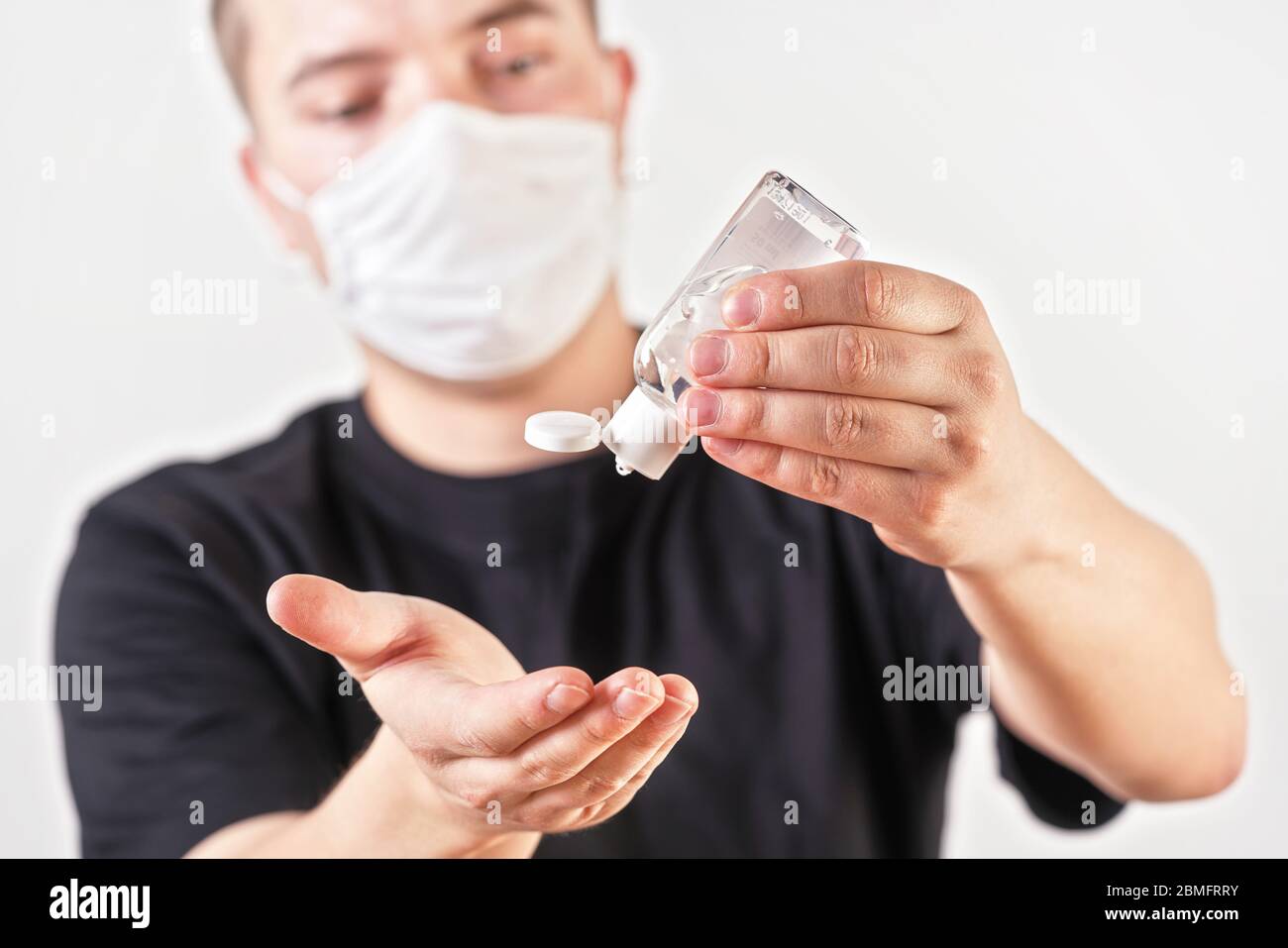 Junge Mann Hände halten antibakterielle Reibgel über zu fallen und reinigen, verschwommenes Gesicht mit Mund Nase Maske im Hintergrund. Kann als Coronavirus verwendet werden Stockfoto