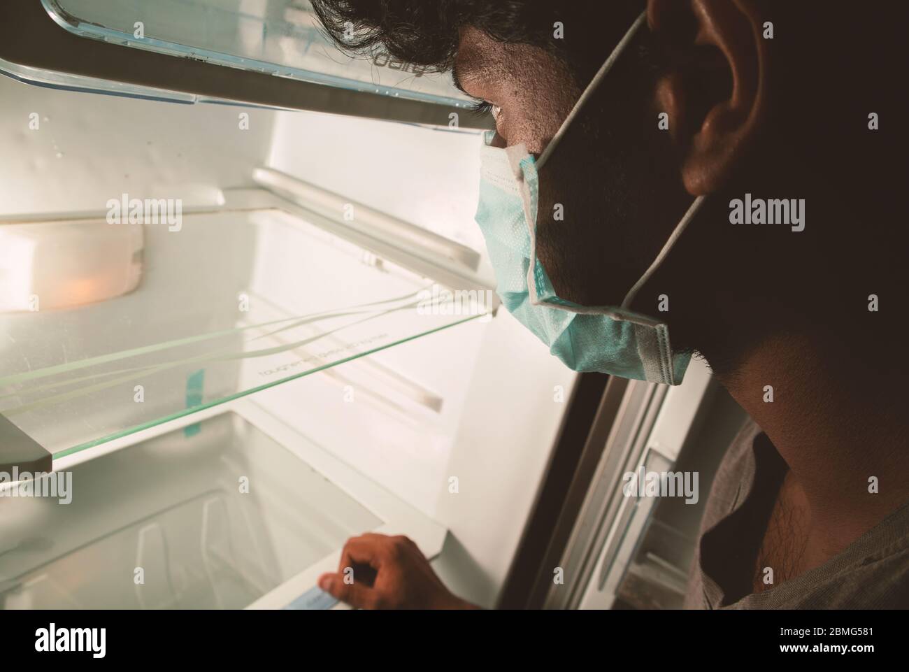 Konzept der Nofood während der Quarantäne zu Hause bei covid-19 oder Coronavirus Pandemie - Mann in medizinischen Maske Blick in leeren Kühlschrank oder Kühlschrank Stockfoto