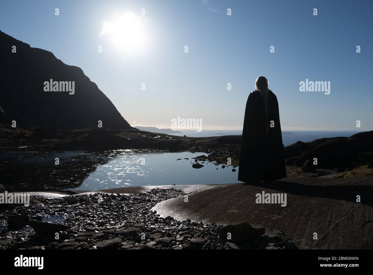 Eine getarnte Figur, in Kontemplation verloren neben einem bergloch, mit Blick aufs Meer Stockfoto