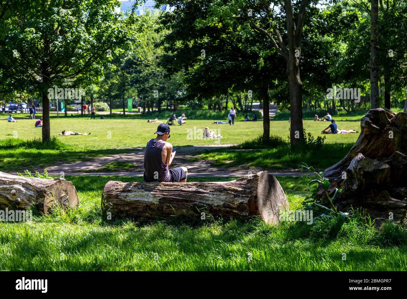 9. Mai 2020, London, Großbritannien - Mann, der auf das Mobiltelefon im Mile End Park schaut an einem Wochenende im heißen Frühling während des Ausbruchs der Coronavirus-Pandemie sonnen sich die Menschen trotz der Einschränkungen der staatlichen Lockdown im Park Stockfoto