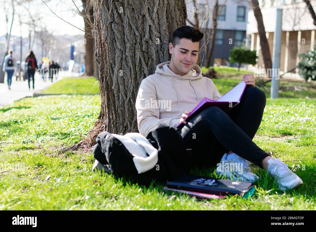 Teenager, der auf dem Schulgras sitzt, während er mit einem Buch studiert Stockfoto